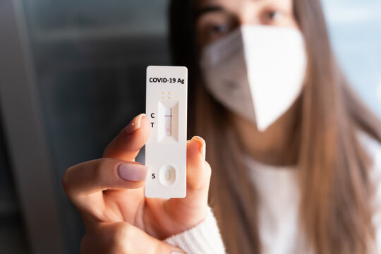 Woman with mask holding a negative self home test with negative result. Corona virus - Covid-19 rapid test. Young teenager girl.