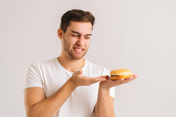 Close-up portrait of displeased young man with disgust pointing to bad burger on white isolated...