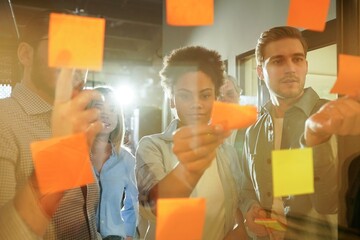 Diverse group of businesspeople standing in an office brainstorming together with sticky notes on a...