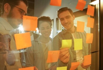 Diverse group of businesspeople standing in an office brainstorming together with sticky notes on a...