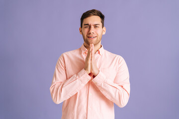 Portrait of excited young man holding hands folded in prayer beg about something make wish keep...