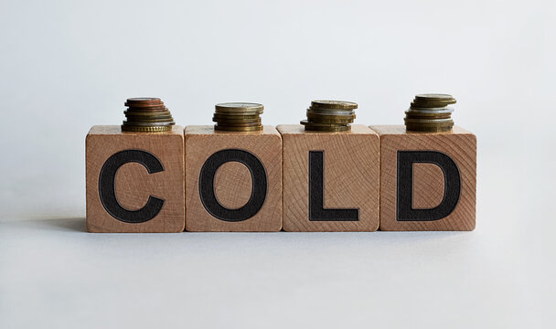 COLD inscription on wooden cubes, together with coins, isolated on white background, business and finance concept.