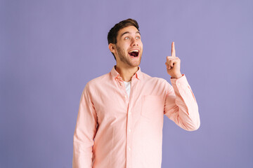 Portrait of happy young man thinking about something and having idea moment pointing finger up on pink isolated background. Cheerful male showing eureka gesture in studio. - obrazy, fototapety, plakaty