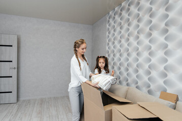 A young mother with children unpacks a box of things after moving to a new apartment. Purchase of real estate. Housewarming, delivery and transportation of goods.