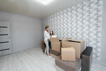 Fototapeta premium A young mother with children unpacks a box of things after moving to a new apartment. Purchase of real estate. Housewarming, delivery and transportation of goods.
