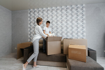 A young mother with children unpacks a box of things after moving to a new apartment. Purchase of real estate. Housewarming, delivery and transportation of goods.