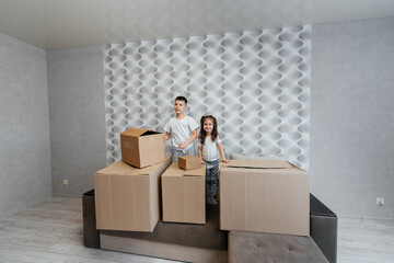 Brother and sister are playing and enjoying moving to a new apartment against the background of cardboard boxes on the couch. Purchase of real estate. Housewarming, delivery.