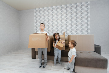 Fototapeta na wymiar Brothers and sister are playing and enjoying moving to a new apartment against the background of cardboard boxes and a sofa. Purchase of real estate. Housewarming, delivery.