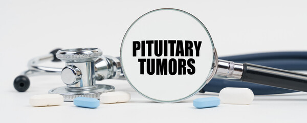 On a white surface are pills, a stethoscope and a magnifying glass inside which is written -...