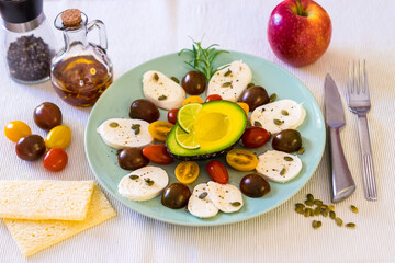 Fresh caprese salad. A dish with cheese mozzarella and cherry tomatoes, pepper and pumpkin seeds. Half an avocado and a red apple to complement a healthy vegetarian meal. Healthy Mediterranean diet
