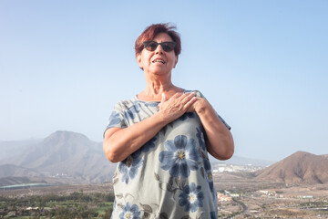 Naklejka premium Adult mature woman with hands in heart, donation, organ donor, thank you concept. Emotional positive kind woman feeling thankful outdoors, showing gratitude sign, believe faith charity concept