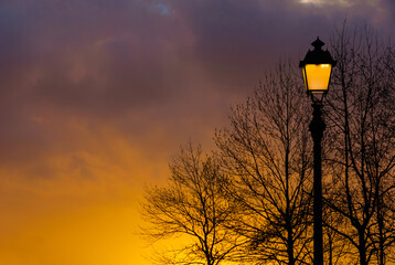 Old fashioned street lamp against beautiful sunset sky and bare tree branches silhouettes (with...