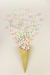 Yellow waffle cone with green, pink and yellow marshmallows on pastel background.