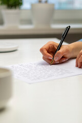 The woman writes a letter. Cropped hands on the table with pen and paper.
