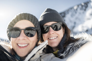 Young friends having fun doing selfie during winter vacation with mountain snow on background - Focus on right girl