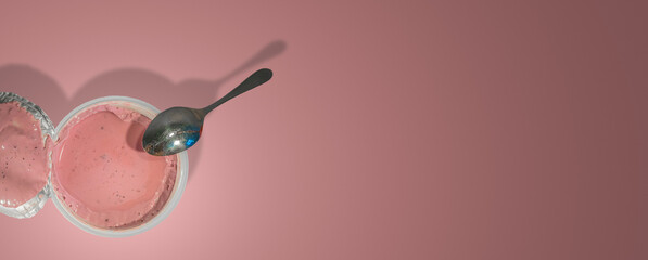 Banner with a fruits yogurt in a plastic packaging and a teaspoon at gradient pink background with...