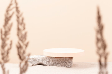 Round beige platform podium on grungy concrete stone on white beach sand with dry bent plant in...