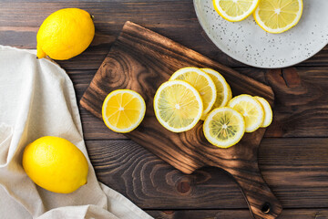 Sliced round pieces of lemon on a cutting board and whole lemons on a wooden table. Organic nutrition, source of vitamins. Top view