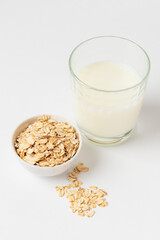 Oats as popular ingredient for variant of vegetable milk. Dry, raw oat flakes in boul and milk in a glass ingredients for making oatmeal porridge on  white background