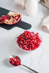 Grains of a ripe pomegranate in a bowl and in a spoon and a part of a pomegranate on a light table. Organic natural food. Vertical view. Close-up