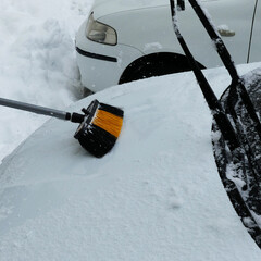 cleaning the snow accumulated on the car with a brush, snow falling on the car in winter,