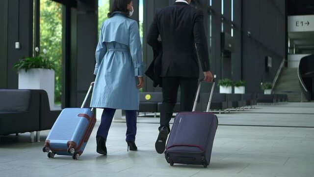 Young businessman, businesswoman walking at airport and talking with suitcases in hands spbd. Back view of American African man, woman walk in lobby and talk with smiles, move luggage and wait for