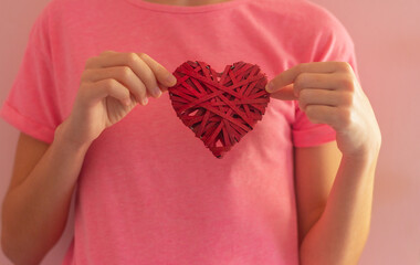 a girl holds a red wicker heart with her hands in front of her. concept of love, valentine's day and romance. health, heart disease and care