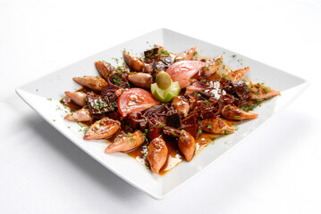 Grilled squid and baby squid with sauce accompanied by tomato and lemon served on a square plate on a white background