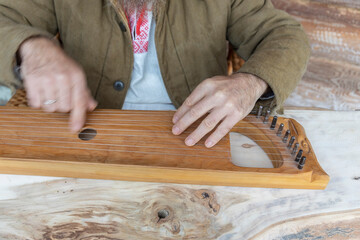 A man in ethnic clothes plays an ancient musical instrument. A man in a brown linen quilted jacket...