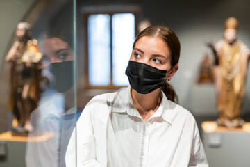 Fototapeta na wymiar Young woman wearing face mask observing artworks in museum