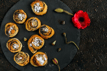 Small homemade buns with poppy seeds and powdered sugar on black slate. Overhead view, selective focus