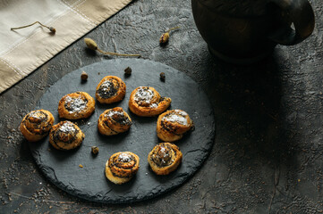 Rolled poppy seed buns on black slate with copy space. Selective focus, natural light