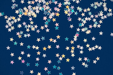 Festive background with holographic sparkling stars confetti on dark blue background. Christmas,...