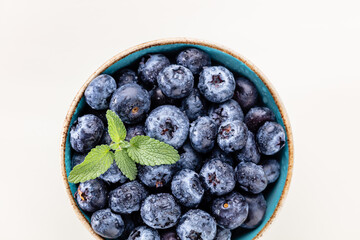 Ripe blueberries with water drops in a bowl on a pastel background,