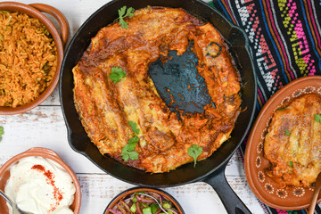 Bean enchiladas served in traditional cast iron skillet and clay dishes, white wooden table