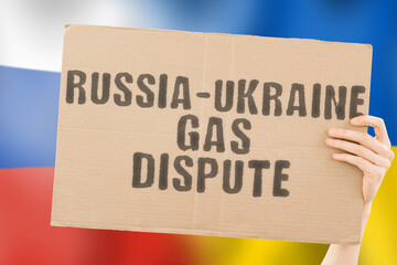 The phrase " Russia-Ukraine gas.dispute " on a banner in men's hand with blurred Ukrainian and Russian flag on the background. Conflict. Economy. Confrontation. Illegal. War. Relationship