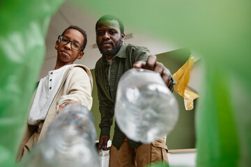 Low angle view at father and son sorting household waste at home together, recycling bin POV