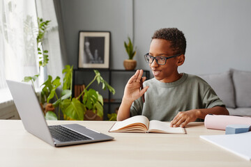 Obraz premium Portrait of smiling African-American boy wearing glasses watching online lessons while studying at home, homeschooling concept, copy space