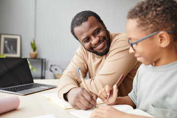 Portrait of happy African-American father helping son with homework while studying at home