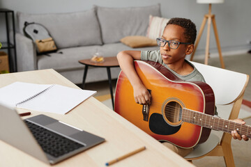 Portrait of young African-American boy learning to play guitar in online lesson, copy space