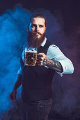 bearded man holds tasty draft beer in hand over smoke background. Drinking, October fest concept. 
