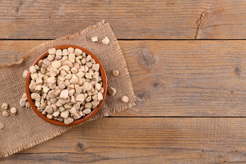 Obraz na płótnie Canvas Dry raw cicerchia or indian pea on a clay plate with burlap napkin on natural wooden background, top view copy space. Legumes known as Lathyrus Sativus, Chickling Vetch, Blue Sweet Pea, made in Puglia