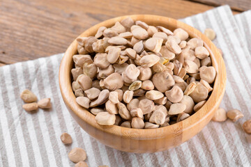 Dry raw cicerchia or indian pea on a wooden bowl with napkin on natural wooden background, close up. Legumes known as Lathyrus Sativus, Chickling Vetch, Blue Sweet Pea, made in Puglia