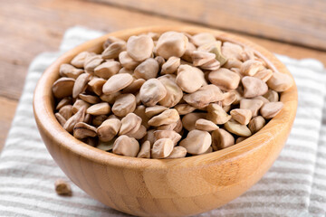 Dry raw cicerchia or indian pea on a wooden bowl with napkin on natural wooden background, close up. Legumes known as Lathyrus Sativus, Chickling Vetch, Blue Sweet Pea, made in Puglia