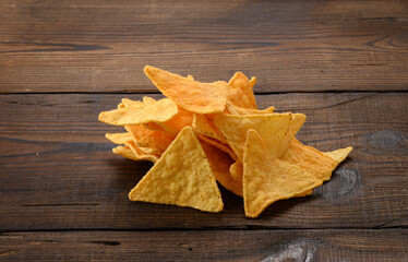 pile of corn tortilla chips or nachos on a brown wooden background, close up