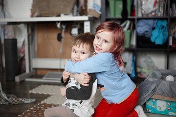 Little caucasian girl hugging with her brother on the floor in their room