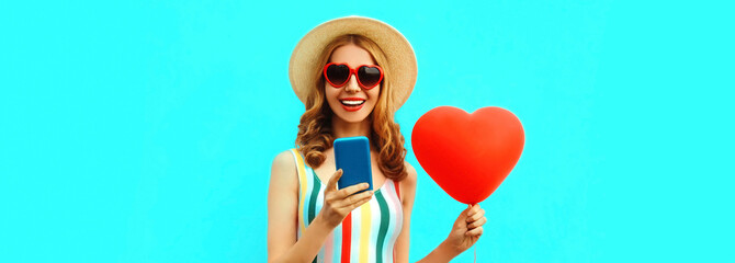 Portrait of happy smiling young woman with phone and red heart shaped balloon wearing a summer...