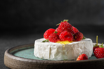 Brie or camembert cheese with raspberry, strawberry, honey and thyme on dark background. French...