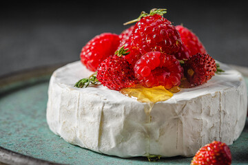Camembert or brie cheese with wild berries, honey and thyme on dark background. French appetizer...