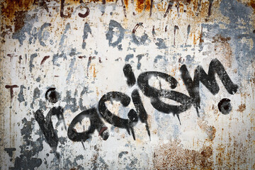 The word racism spray painted on grungy concrete background. Weather washed.